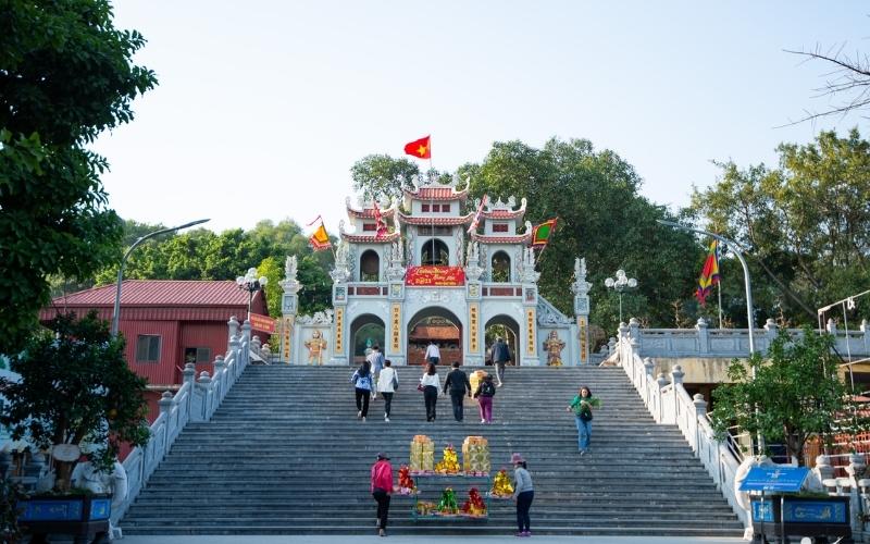Entrée du temple de Bà Chúa Kho à Bắc Ninh, avec un large escalier en pierre menant à une porte monumentale décorée de drapeaux et d’inscriptions, où des visiteurs montent pour faire leurs offrandes