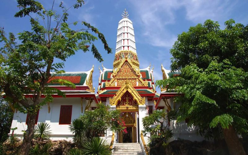 Vue extérieure du temple Wat Chakrawat, avec son architecture traditionnelle thaïlandaise ornée de dorures, de toits colorés et d'une grande tour blanche en arrière-plan