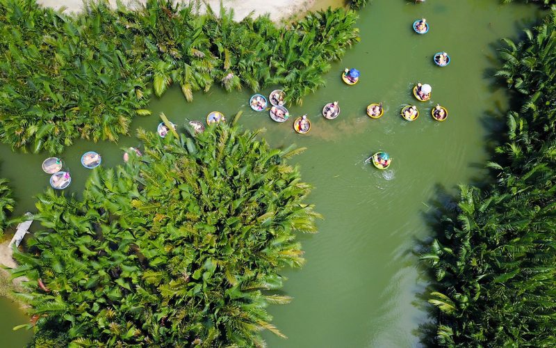 Vue aérienne du village de cocotiers de Cam Thanh à Hoi An, avec des touristes naviguant sur la rivière dans des bateaux paniers traditionnels entourés de palmiers d’eau luxuriants