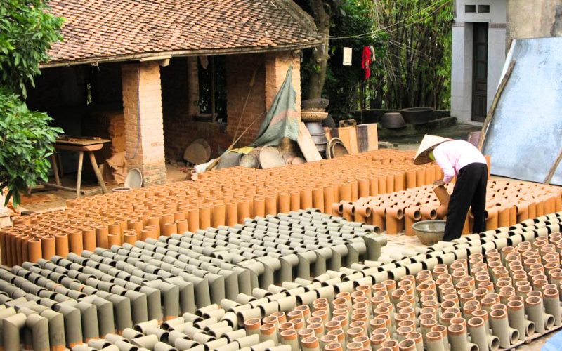 Artisan au village de poterie de Phù Lãng à Bắc Ninh, disposant des pièces en argile façonnées pour les faire sécher au soleil devant un ancien atelier en briques
