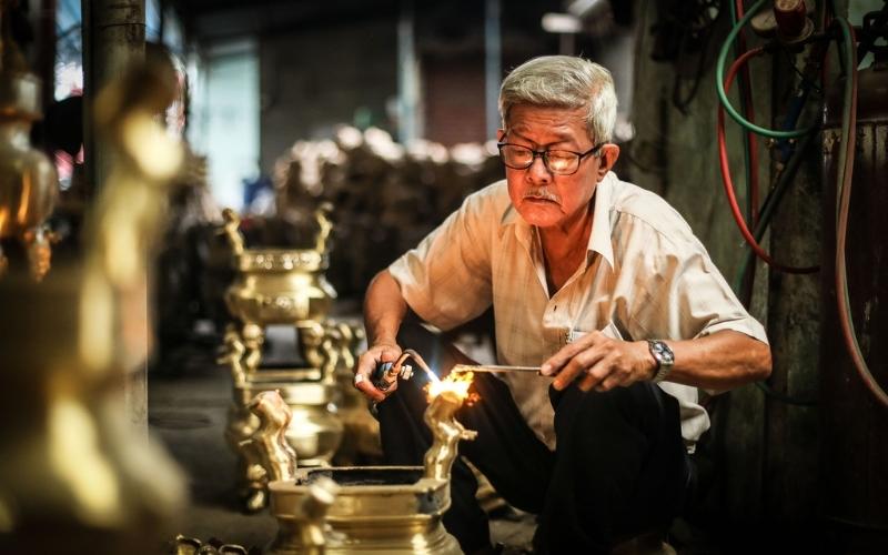 Artisan du village de Đại Bái à Bắc Ninh travaillant le bronze, concentré sur le polissage et la finition d’un objet traditionnel en métal dans son atelier
