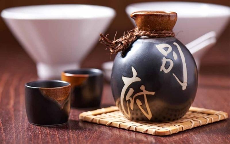 Bouteille traditionnelle de rượu làng Vân (alcool de riz de Bắc Giang), en céramique noire décorée de caractères chinois, accompagnée de petites tasses et posée sur un dessous en bambou