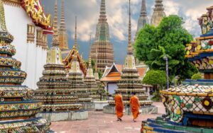Vue du temple Wat Pho à Bangkok, avec ses stupas colorés et des moines marchant dans la cour