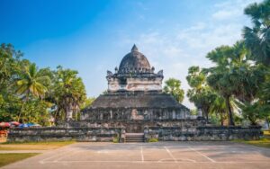 Stupa ancienne de Wat Visoun à Luang Prabang, entourée de palmiers et d'une cour paisible sous un ciel bleu
